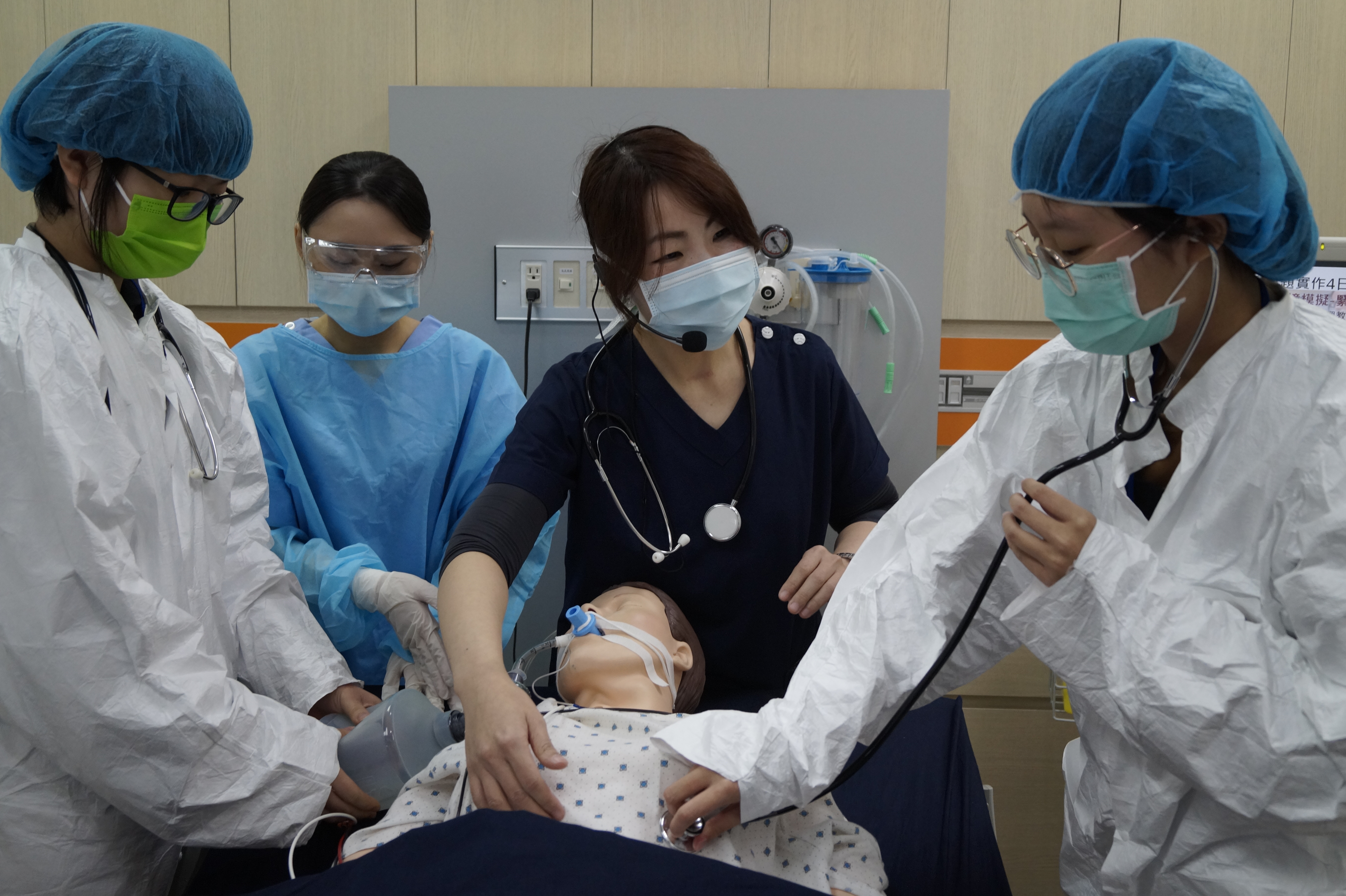 圖說：亞大護理學系彭逸稘老師（中），利用智慧高階模擬人，設定緊急救護擬真情境，讓學員們（左、右戴藍色帽子者）體驗。