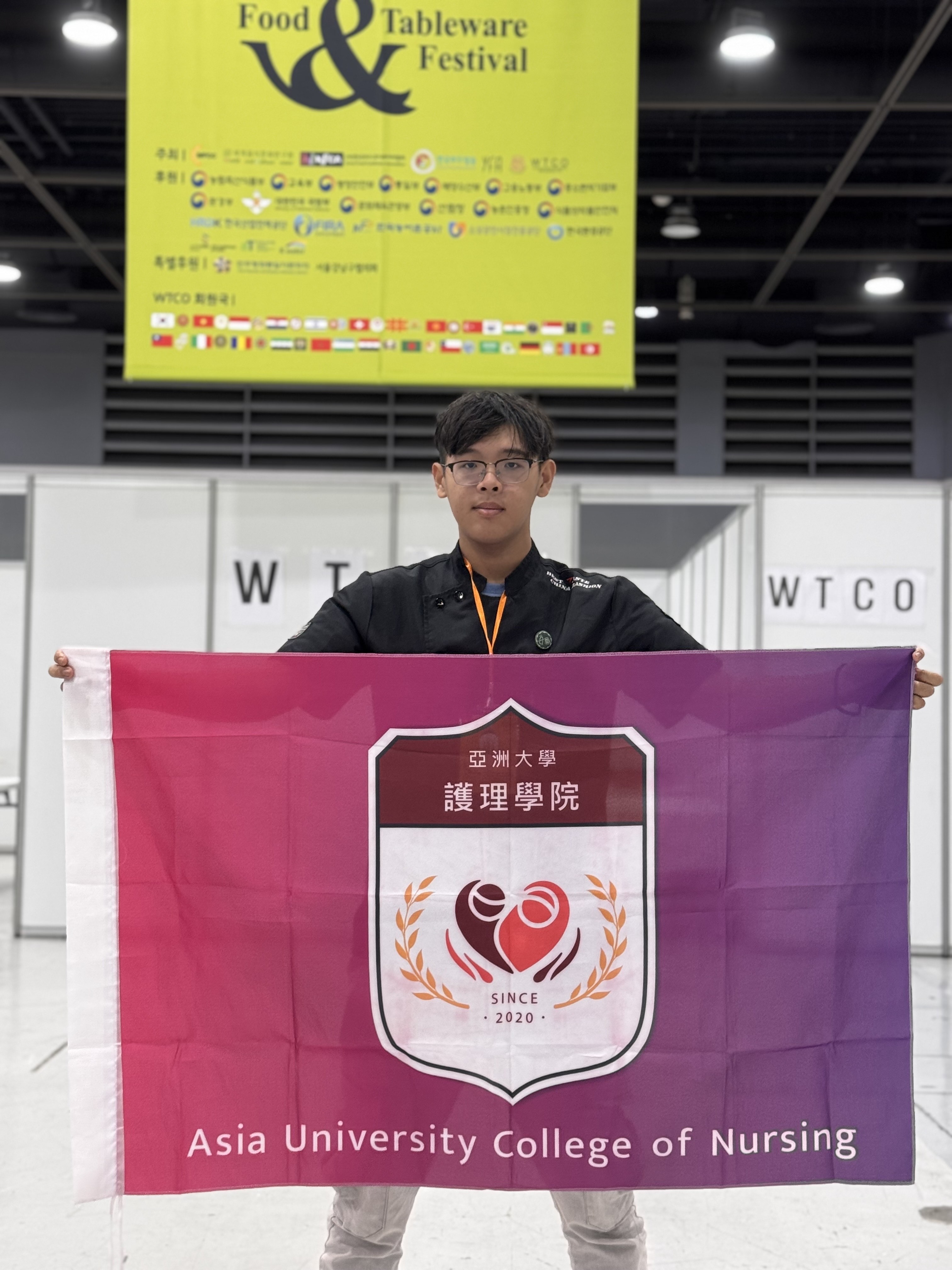 圖說：亞大護理學系林明宏同學於韓國首爾aT會展中心高舉護理學院院旗拍照。